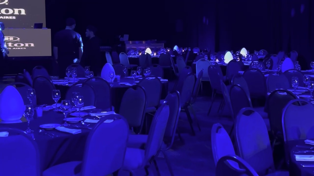 Cena de gala en un salón del Hilton con iluminación azul y estructura de luces sobre las mesas