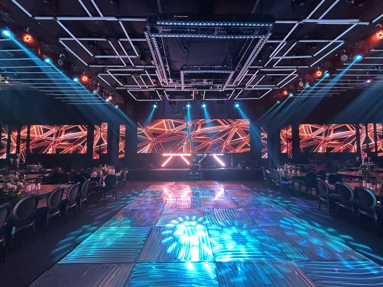Salón con pista de baile iluminada, pantallas LED y estructura de luces